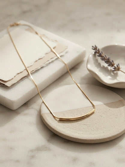 Minimalist gold curved bar necklace.