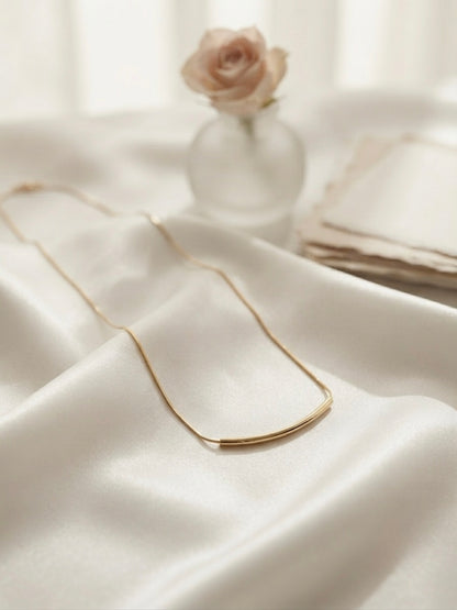Minimalist gold curved bar necklace.